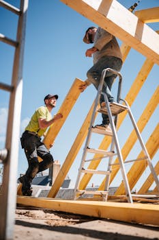Two construction workers building a wooden roof structure on a sunny day.